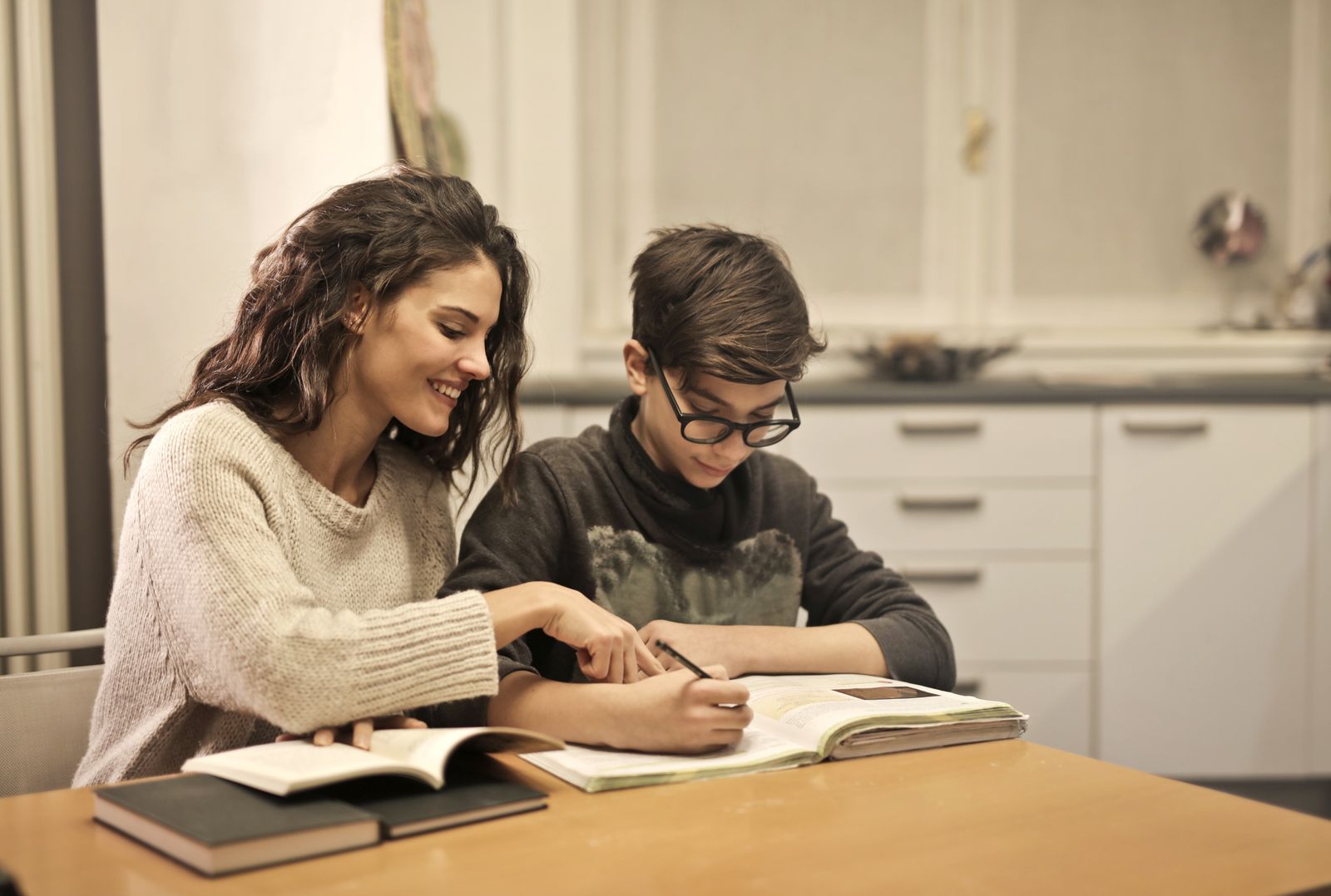 An adult helping a young person with homework at a kitchen table